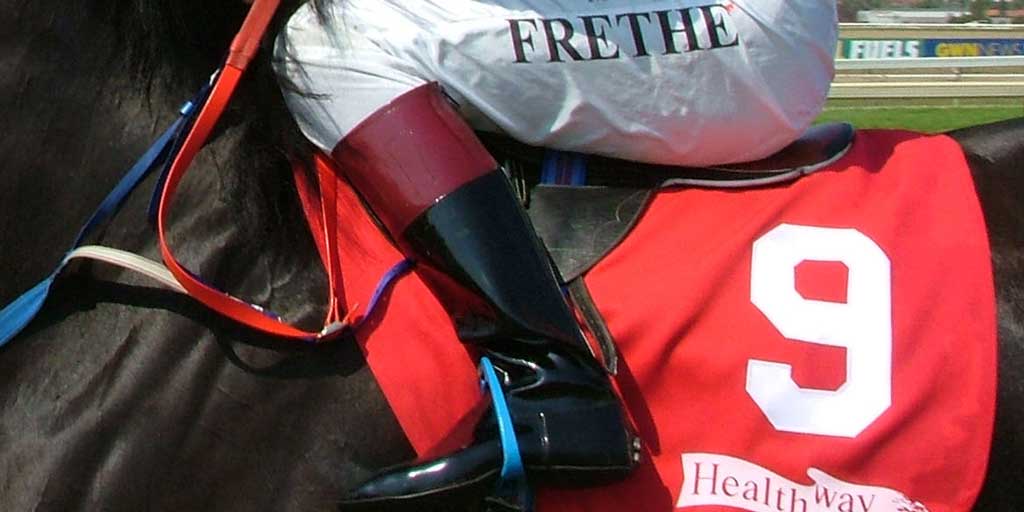 A closeup of a jockey sitting in the saddle of a handicapped race horse with the number nine.